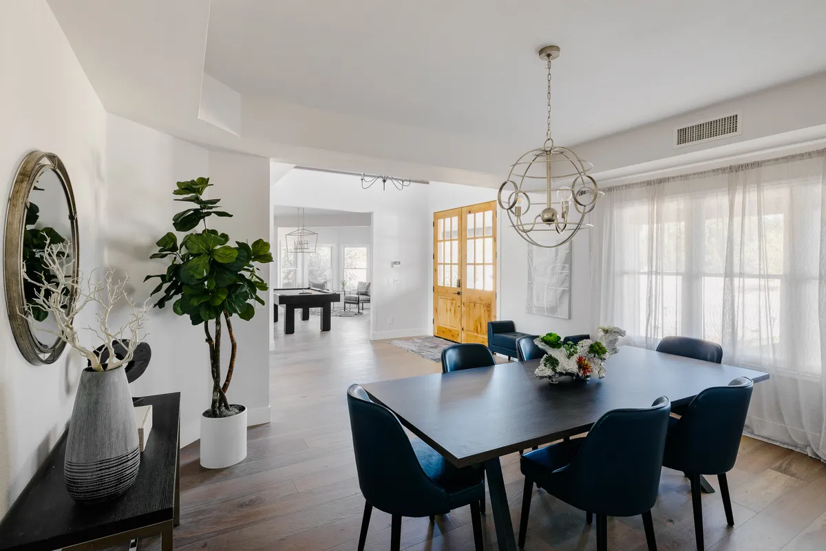 A modern dining area with a stylish dining table, an elegant chandelier, large windows, and a decorative plant. The setting exudes an inviting and cozy atmosphere perfect for celebratory dinners and everyday family gatherings.