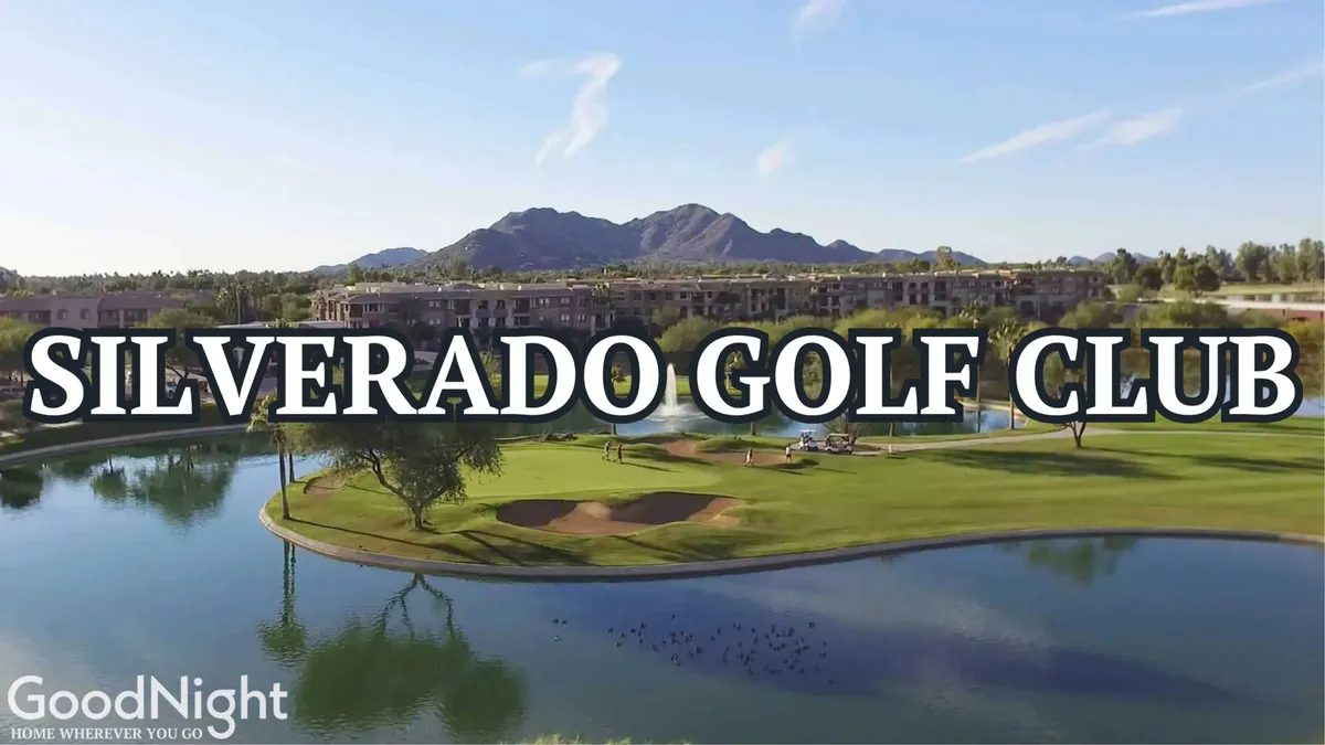 A sweeping view of a lush golf course bordered by a tranquil pond, with resort-style buildings and dramatic mountains in the background. The scene is bathed in warm sunlight, conveying a relaxing and leisurely atmosphere ideal for golf enthusiasts.