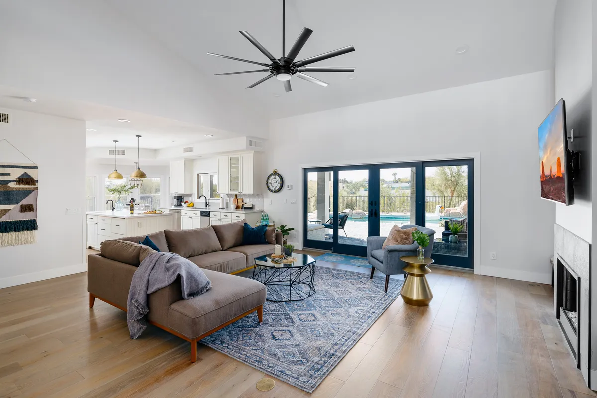 A warm and inviting living space featuring a plush sofa, a coffee table, a soft rug, and large windows that fill the room with natural light. The kitchen area is visible in the background, illustrating the open-concept design and seamless flow between living and dining spaces.