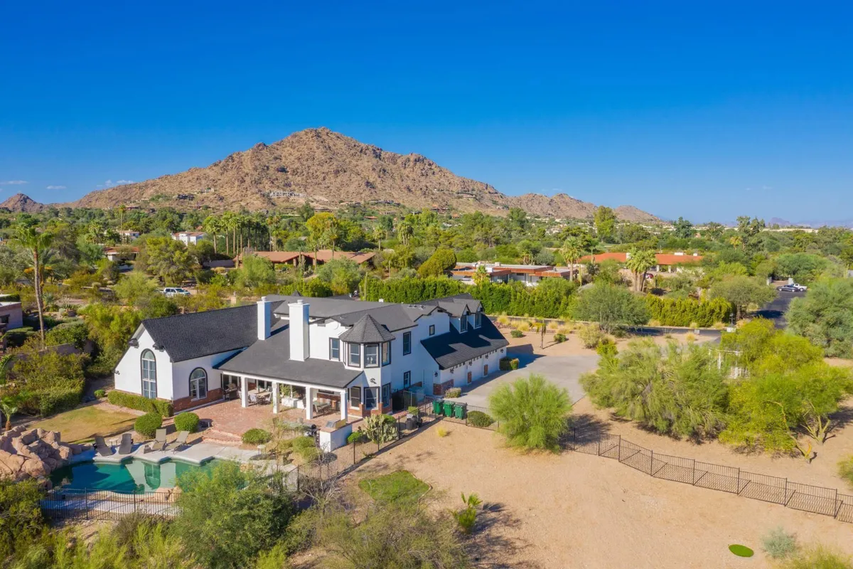 A luxurious estate with a sparkling swimming pool sits against a dramatic mountain backdrop. The landscaped garden and inviting patio provide ample outdoor space for group gatherings, relaxation, and networking. The grand architecture and setting evoke exclusivity and tranquility.