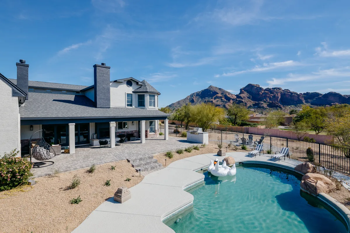 The hero image showcases a luxurious swimming pool surrounded by a spacious patio with comfortable outdoor seating. Beyond the pool, sweeping views of Camelback Mountain create a dramatic natural backdrop, while the serene atmosphere invites relaxation and outdoor enjoyment.