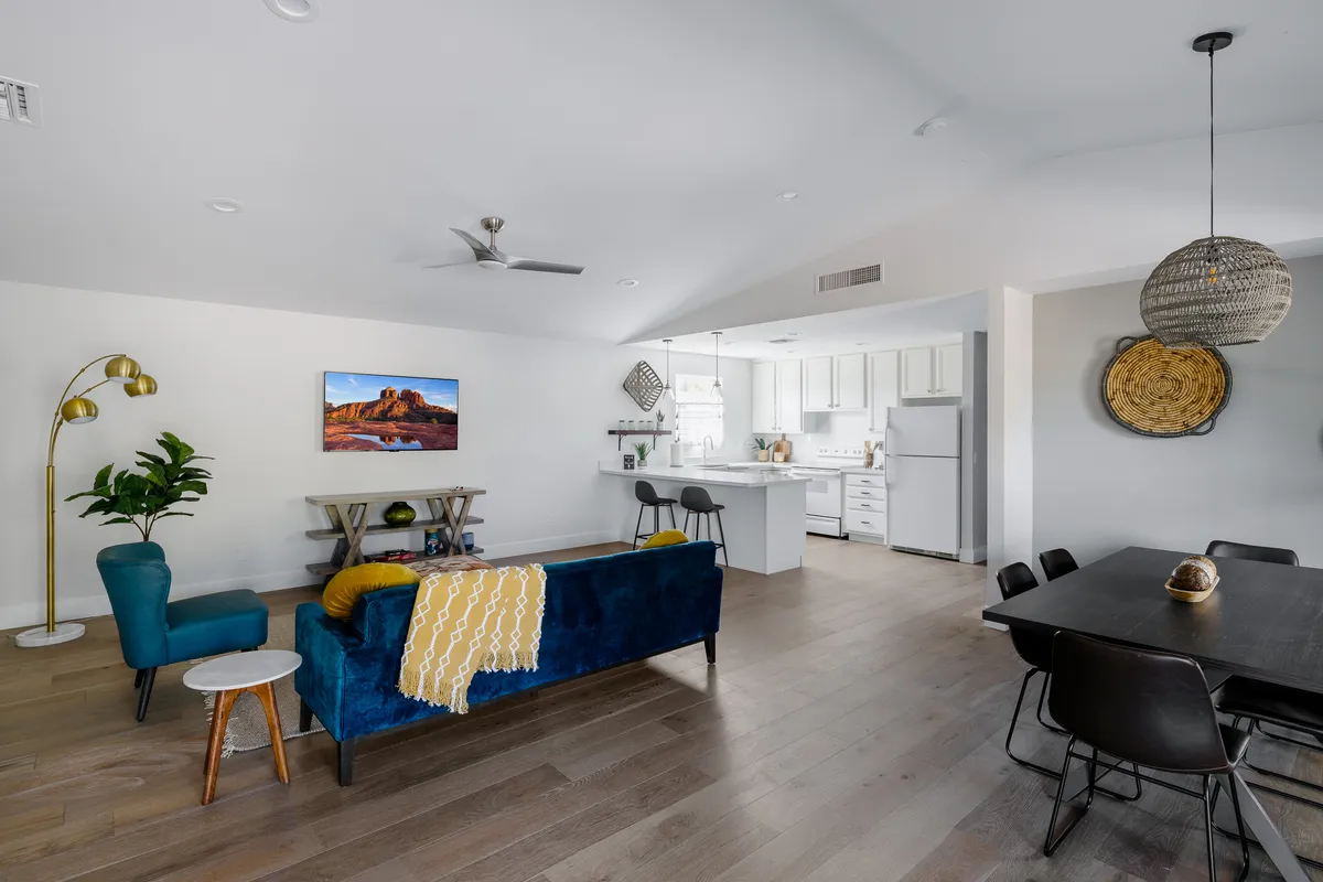 An open-concept guest house area featuring a blue couch, yellow throw, kitchen island, dining table, and wall art. The space feels welcoming and multi-functional, perfect for both relaxing and entertaining.